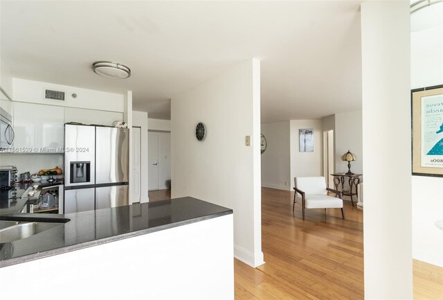 kitchen with appliances with stainless steel finishes, dark stone countertops, kitchen peninsula, and light wood-type flooring