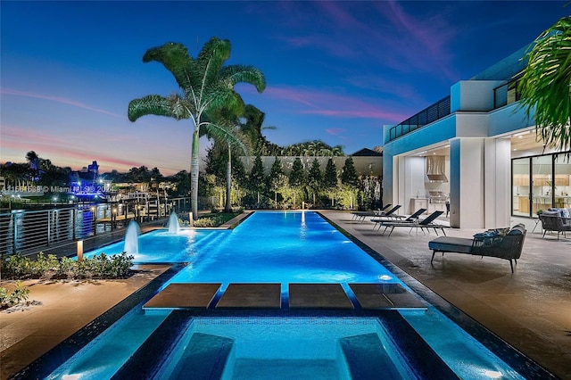 pool at dusk with an in ground hot tub, pool water feature, and a patio