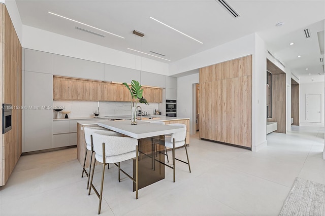 kitchen with tasteful backsplash, a center island with sink, a kitchen bar, and light brown cabinets