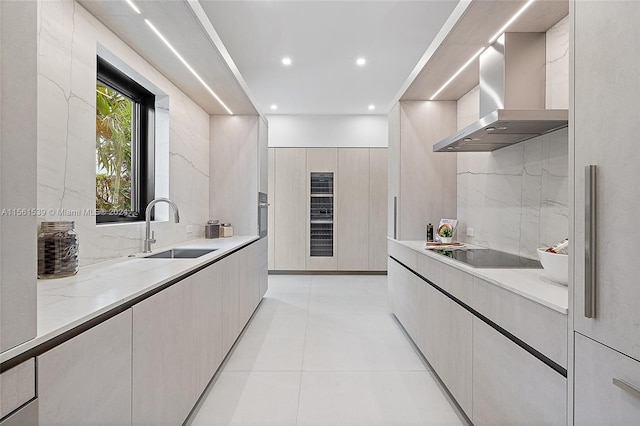 kitchen with backsplash, black electric stovetop, sink, wall chimney exhaust hood, and light tile patterned floors