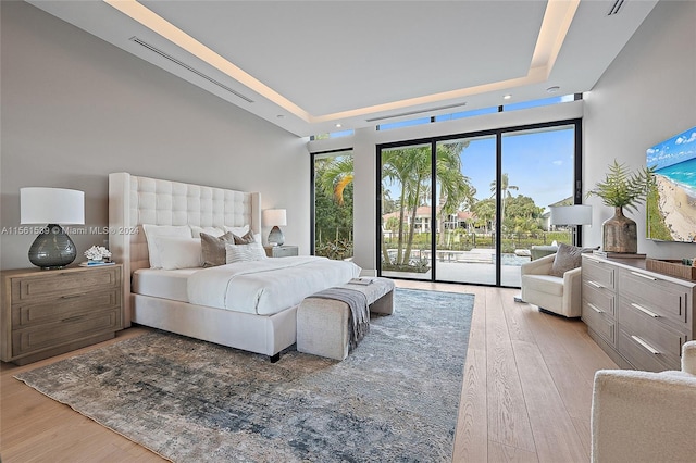 bedroom featuring access to exterior, a tray ceiling, and light hardwood / wood-style flooring