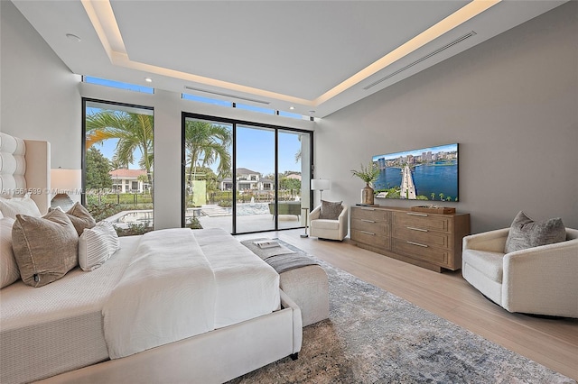 bedroom featuring access to exterior, light hardwood / wood-style floors, and a raised ceiling