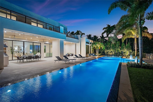 pool at dusk with a patio and ceiling fan