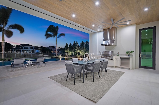 patio terrace at dusk with a grill, ceiling fan, and an outdoor kitchen