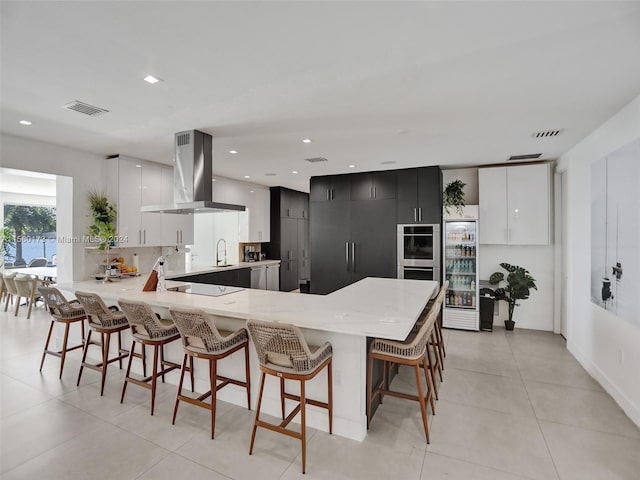 kitchen featuring a breakfast bar, double oven, light tile flooring, and island exhaust hood