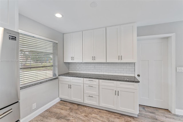 kitchen featuring dark stone counters, stainless steel fridge, white cabinetry, and decorative backsplash