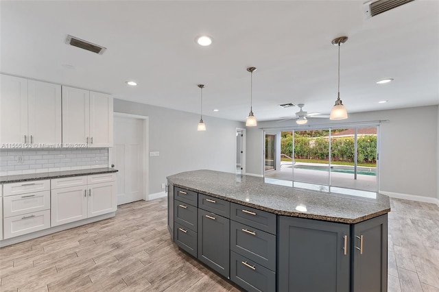 kitchen with white cabinets, light hardwood / wood-style floors, hanging light fixtures, ceiling fan, and dark stone counters