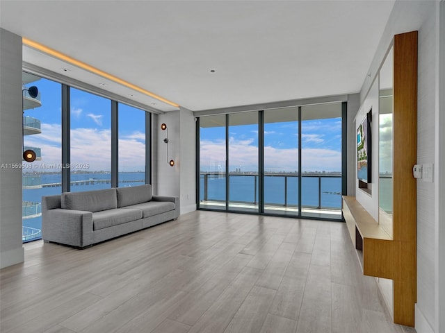 unfurnished living room featuring a water view, a wall of windows, and light hardwood / wood-style floors