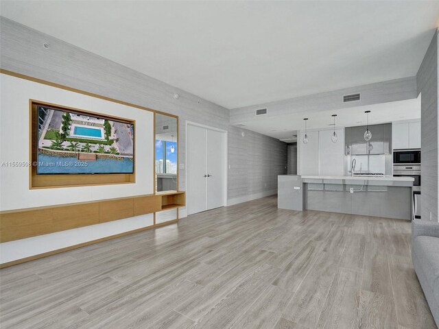 unfurnished living room with sink, a wall of windows, and light hardwood / wood-style flooring