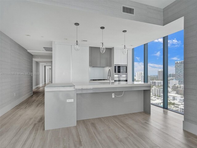 kitchen with pendant lighting, sink, expansive windows, a large island, and white cabinets