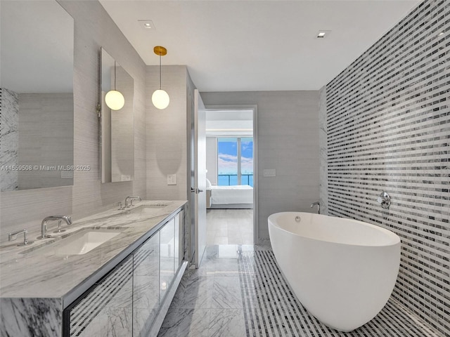 ensuite bathroom featuring a freestanding bath, double vanity, marble finish floor, tile walls, and a sink