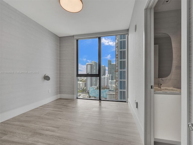 unfurnished room with a city view, a sink, expansive windows, wood finished floors, and baseboards