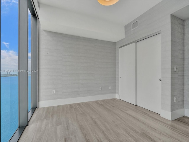 unfurnished bedroom with a wall of windows, a closet, and light hardwood / wood-style flooring