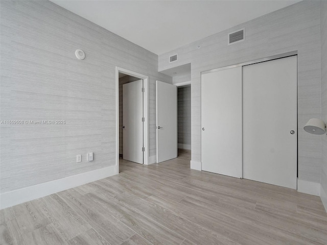 unfurnished bedroom with a closet, visible vents, light wood-type flooring, and baseboards