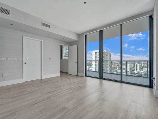 spare room featuring a wealth of natural light, visible vents, light wood-type flooring, and a wall of windows