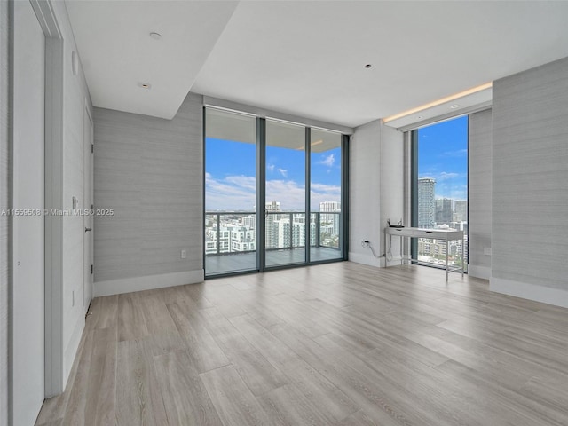 spare room with baseboards, a city view, wood finished floors, and floor to ceiling windows