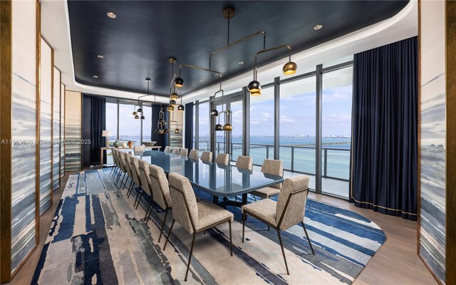 dining room featuring hardwood / wood-style flooring, a wall of windows, a raised ceiling, and a water view