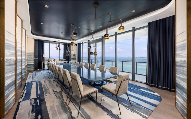 dining area with a tray ceiling, floor to ceiling windows, a water view, and a wealth of natural light