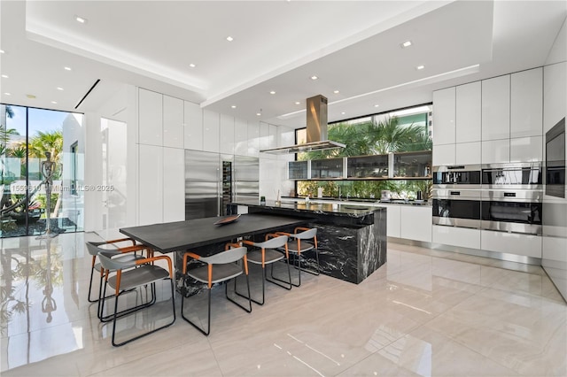 kitchen featuring a kitchen bar, a center island, island range hood, expansive windows, and white cabinets