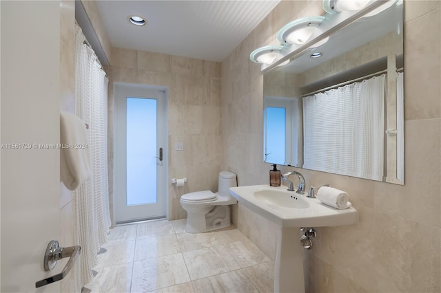 bathroom with toilet, sink, and tile walls