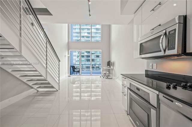 kitchen featuring a high ceiling, stainless steel appliances, light tile floors, and white cabinetry