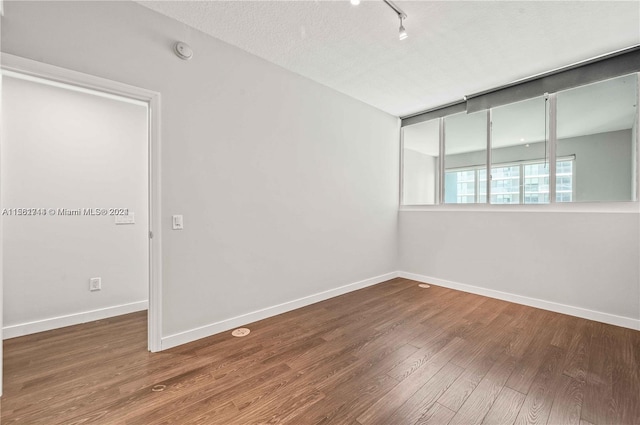 empty room with a textured ceiling, rail lighting, and dark hardwood / wood-style flooring