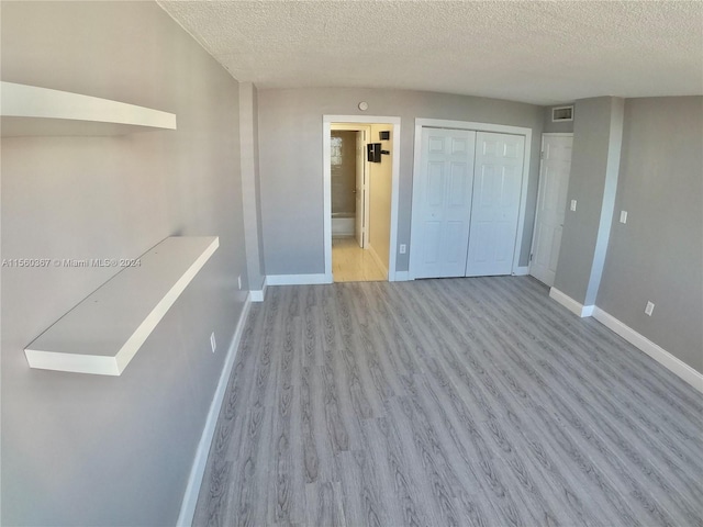 unfurnished bedroom with connected bathroom, a textured ceiling, a closet, and light wood-type flooring