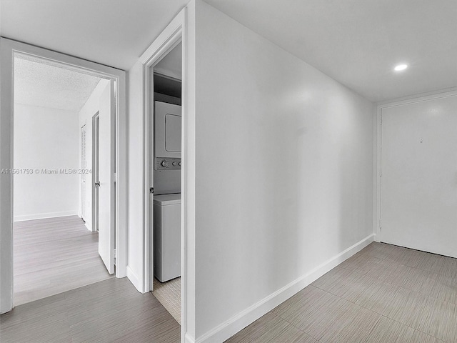 hallway with a textured ceiling and stacked washer / drying machine