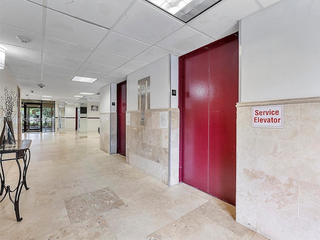 corridor with a paneled ceiling, tile walls, and light tile floors