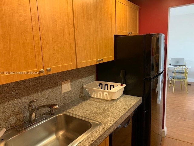 kitchen with black refrigerator, tasteful backsplash, sink, and light hardwood / wood-style flooring