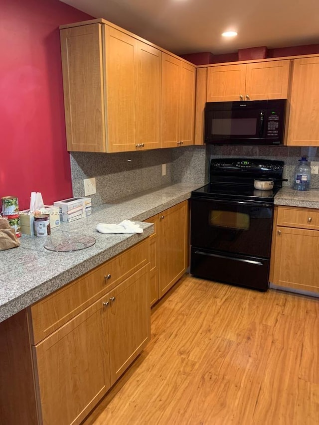 kitchen with light hardwood / wood-style flooring, tasteful backsplash, light stone counters, and black appliances