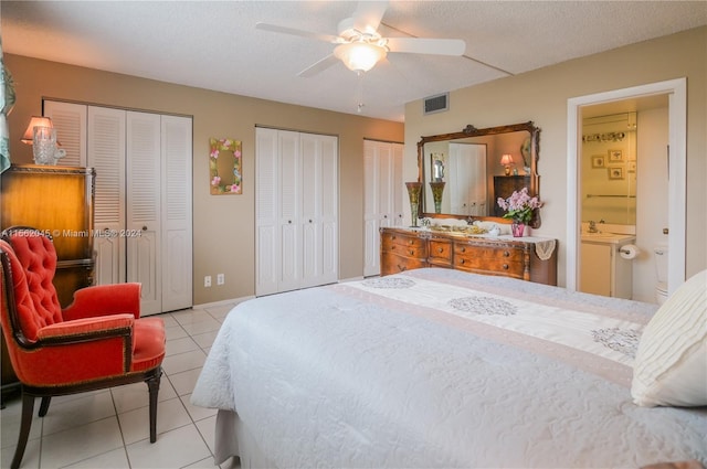 tiled bedroom with ceiling fan, sink, a textured ceiling, ensuite bath, and two closets