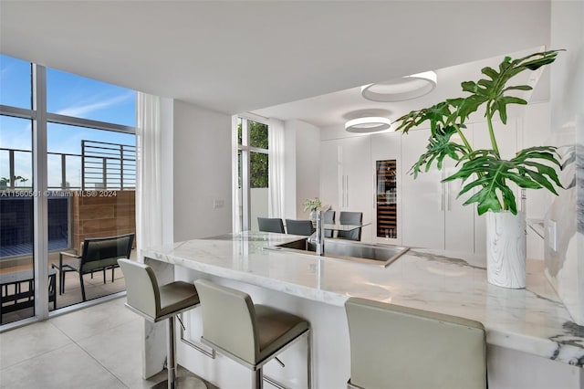 kitchen featuring light stone counters, expansive windows, a kitchen bar, white cabinets, and light tile floors