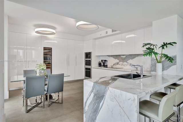 kitchen with stainless steel appliances, backsplash, sink, a breakfast bar area, and white cabinetry