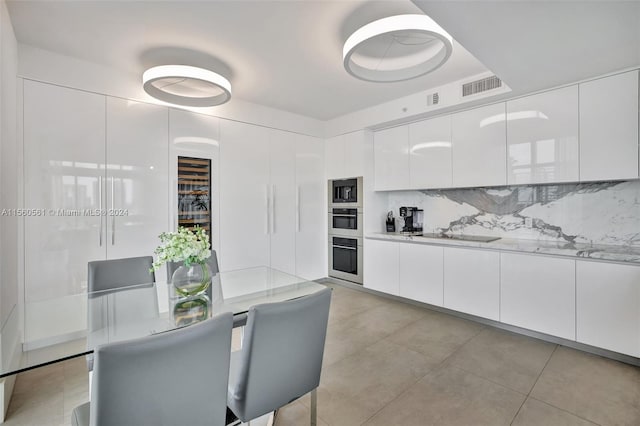 kitchen with light stone counters, light tile flooring, tasteful backsplash, white cabinetry, and appliances with stainless steel finishes