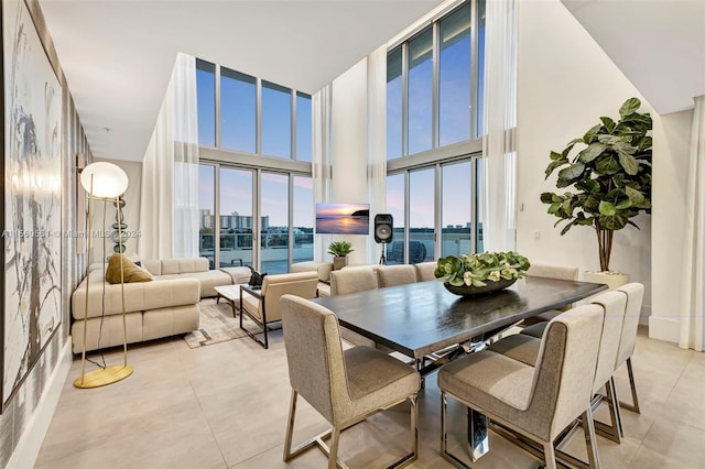 dining area with light tile floors, a high ceiling, a wall of windows, and a water view