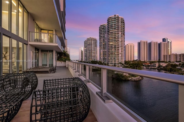 balcony at dusk featuring a water view