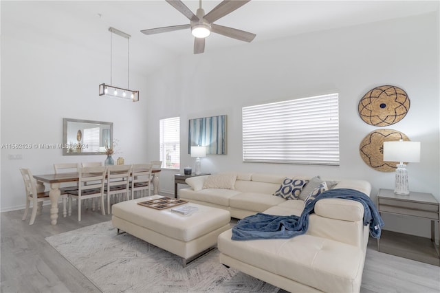 living room featuring high vaulted ceiling, light wood-type flooring, and ceiling fan with notable chandelier