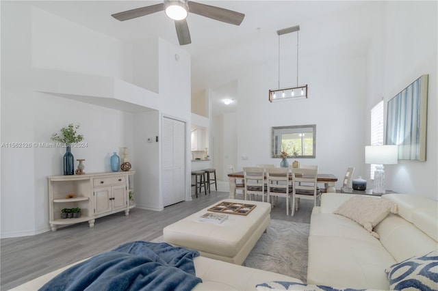 living room featuring a high ceiling, ceiling fan with notable chandelier, and light wood-type flooring