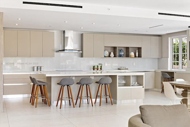 kitchen with decorative backsplash, a kitchen bar, wall chimney exhaust hood, light tile patterned floors, and cream cabinets