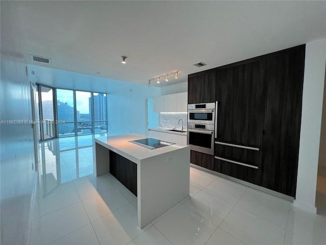 kitchen with rail lighting, an island with sink, sink, and light tile floors