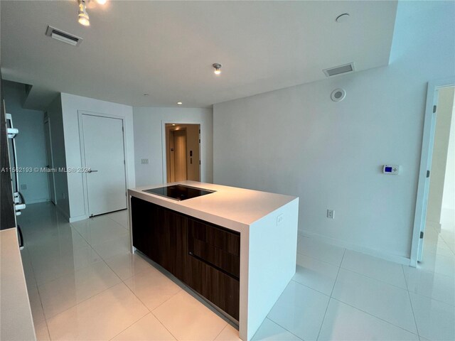 kitchen with a center island with sink, black electric stovetop, light tile floors, and dark brown cabinets