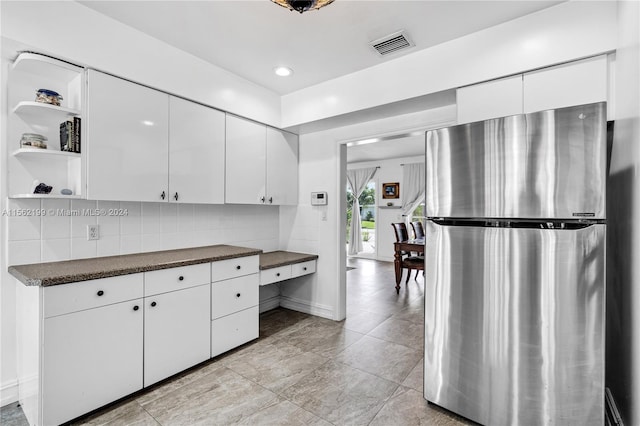 kitchen with backsplash, stainless steel fridge, white cabinetry, and light tile floors