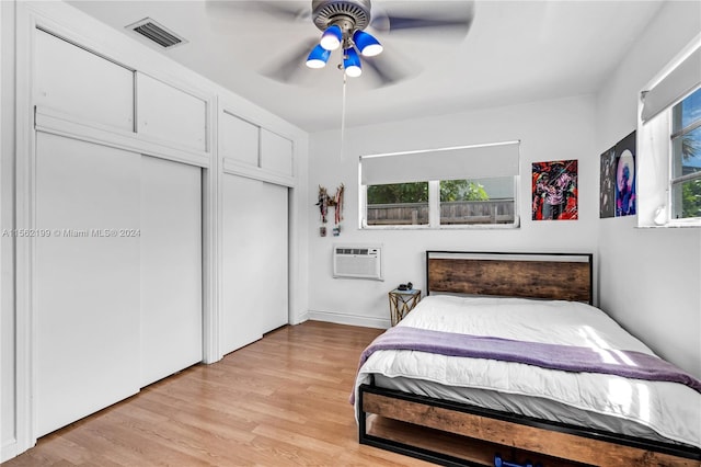 bedroom featuring a wall mounted air conditioner, light hardwood / wood-style floors, and ceiling fan