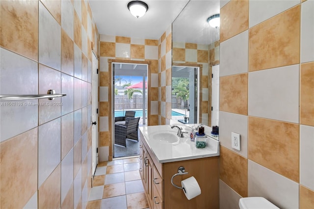 bathroom with tile walls, toilet, large vanity, and tile flooring