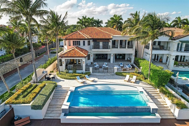 rear view of property featuring a balcony, a patio, and a fenced in pool