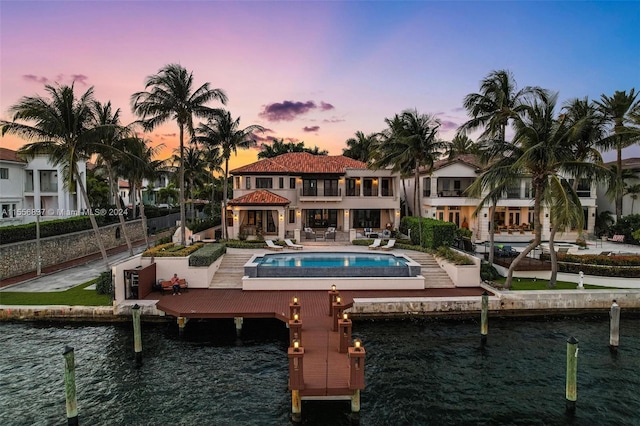 back house at dusk with a patio area, a fenced in pool, and a water view