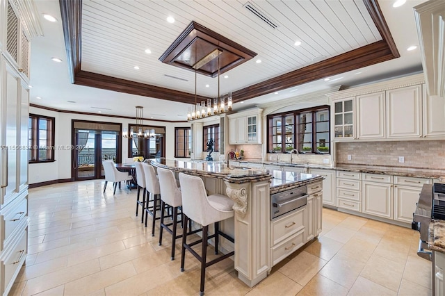 kitchen featuring a chandelier, an island with sink, decorative light fixtures, a kitchen bar, and a tray ceiling