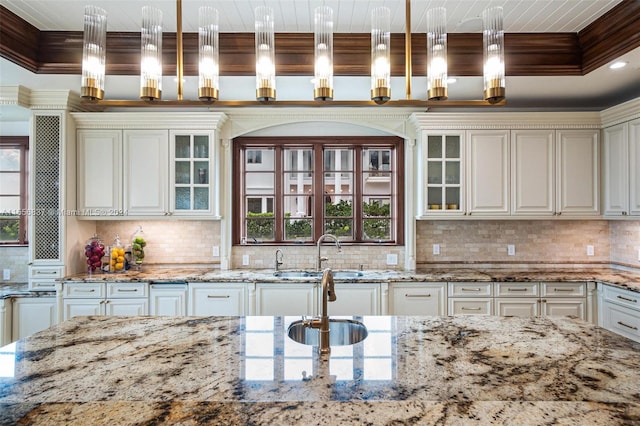 kitchen with backsplash, light stone countertops, decorative light fixtures, and sink