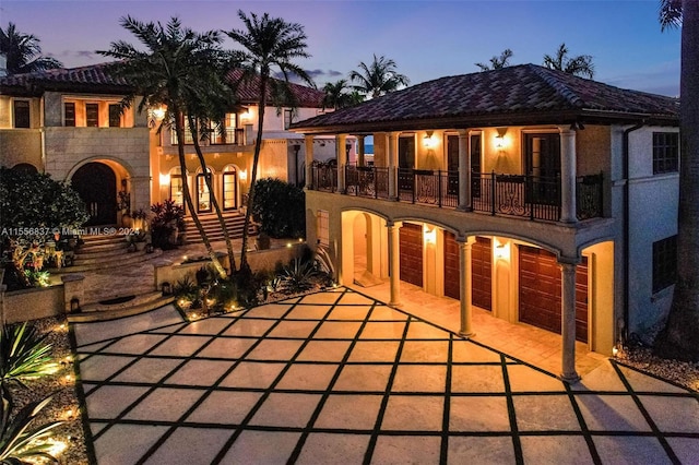 back house at dusk with a balcony and a garage